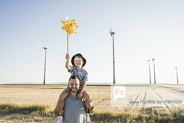 Vater trägt Sohn mit Windrad auf Schultern vor Windkraftanlagen