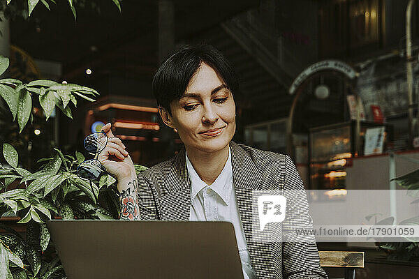Freelancer holding eyeglasses working on laptop at sidewalk cafe