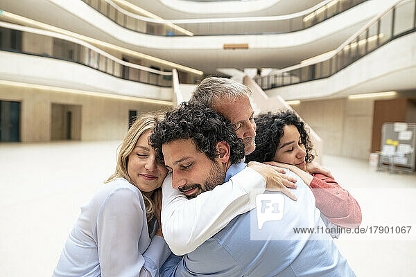 Senior businessman with eyes closed embracing colleagues in lobby