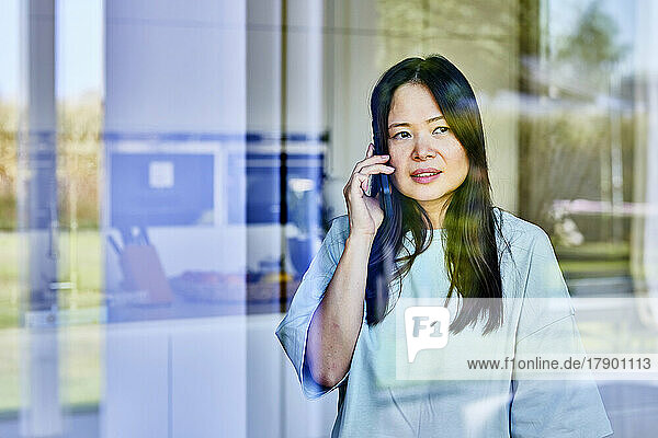 Mature woman talking on smart phone seen through glass