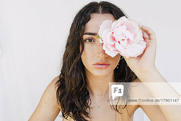 Young woman holding pink flower over eye