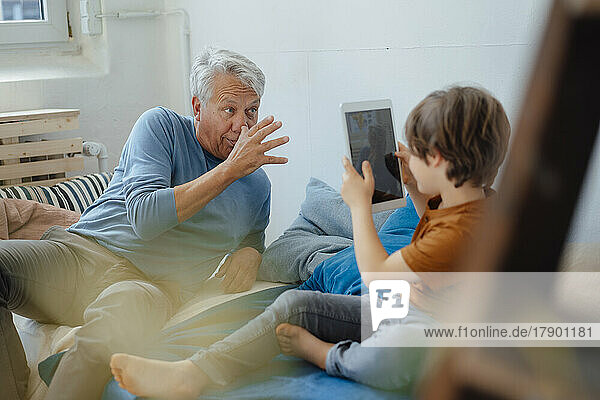 Boy taking picture through tablet PC of playful grandfather teasing at home