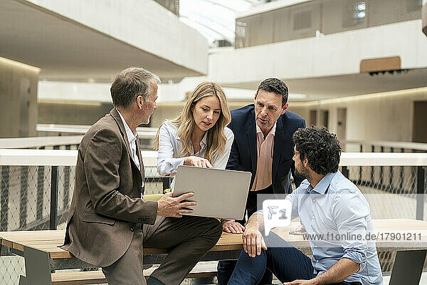 Businesswoman planning strategy over laptop with colleagues in corridor