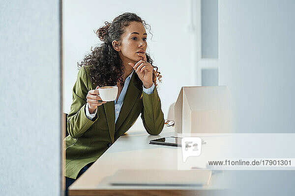 Nachdenklicher Architekt mit Kaffeetasse sitzt am Schreibtisch im Büro