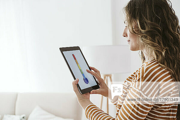 Young woman using digital tablet with thermometer icon in living room