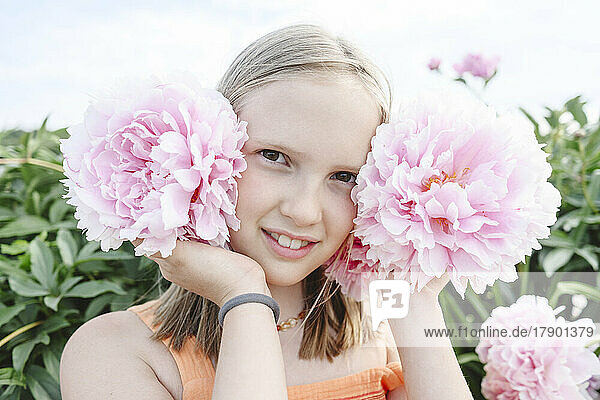 Smiling blond girl holding pink peony flowers