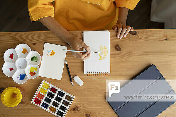 Mädchen malt Aquarelle auf einem Skizzenblock am Tisch
