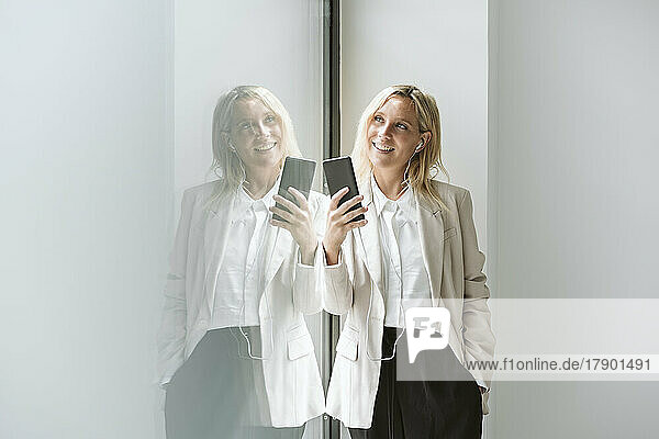 Smiling businesswoman holding mobile phone at glass wall