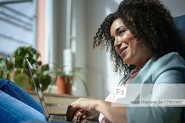 Lächelnde Geschäftsfrau mit Laptop sitzt im Büro