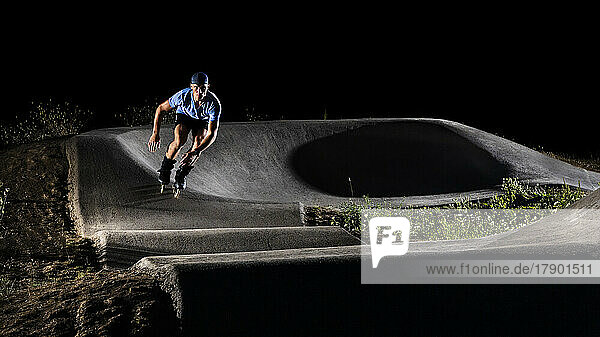 Young man practicing inline skating in skateboard park at night