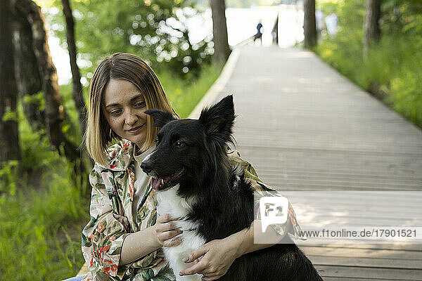 Junge Frau sitzt mit Hund an der Promenade im Park