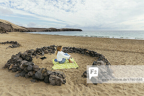 Young woman sitting amidst rocks looking at sea from beach