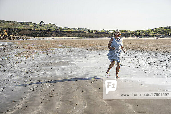 Active senior woman running at beach on sunny day