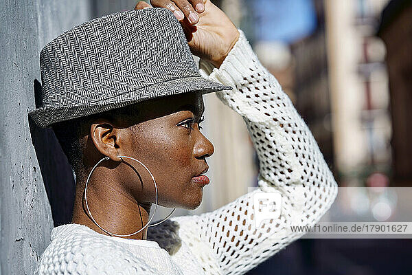 Junge Frau trägt Creolen und Hut an der Wand an einem sonnigen Tag