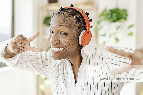 Glückliche Frau mit kabellosen Kopfhörern zeigt zu Hause ein Friedenszeichen