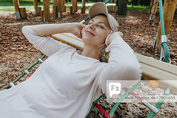 Mature woman listening to music and relaxing on hammock in park