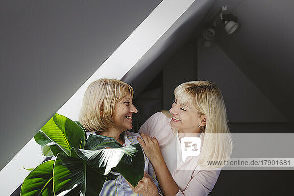 Fröhliche Frau mit Mutter steht zu Hause an der Bananenpflanze