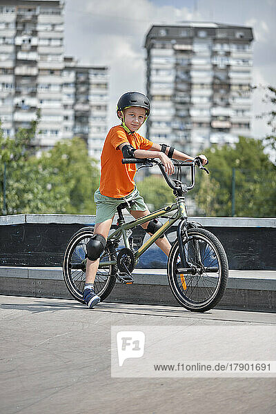 Boy with safety gear sitting on BMX bike at skateboard park
