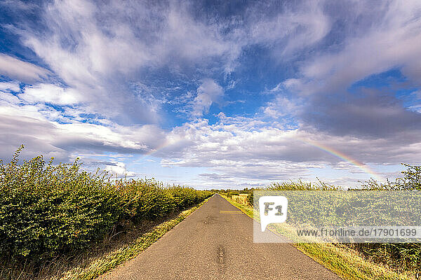 UK  Scotland  Rainbow arching against clouds floating over country road