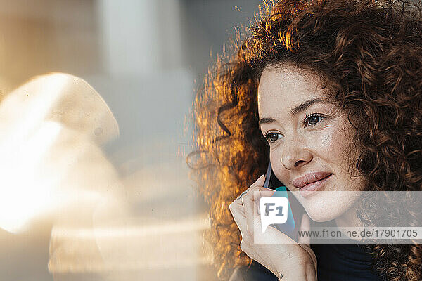 Smiling beautiful woman with curly hair talking on smart phone