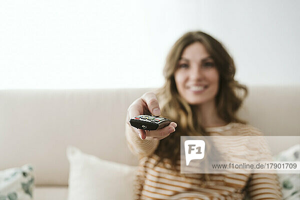 Young woman using remote control on sofa at home