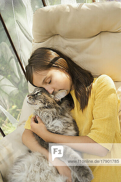 Mädchen mit geschlossenen Augen umarmt Katze auf Hängesessel