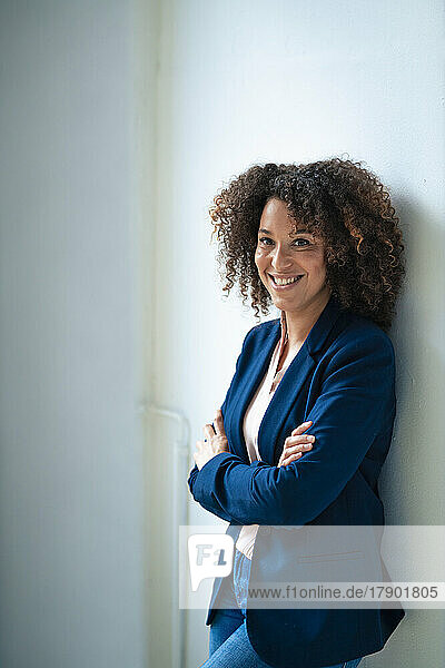 Happy mature businesswoman with arms crossed leaning on wall