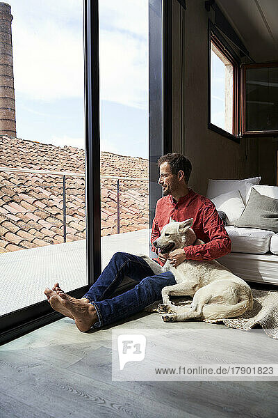 Nachdenklicher Mann sitzt mit Hund und schaut durchs Fenster