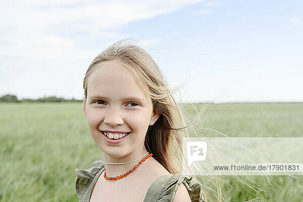 Happy girl with blond hair standing in grassy field