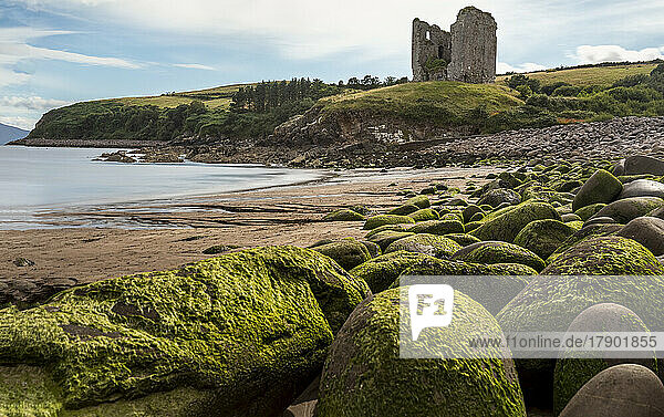 Irland  Kilmurry  am Strand liegende Felsbrocken mit alter Ruine im Hintergrund