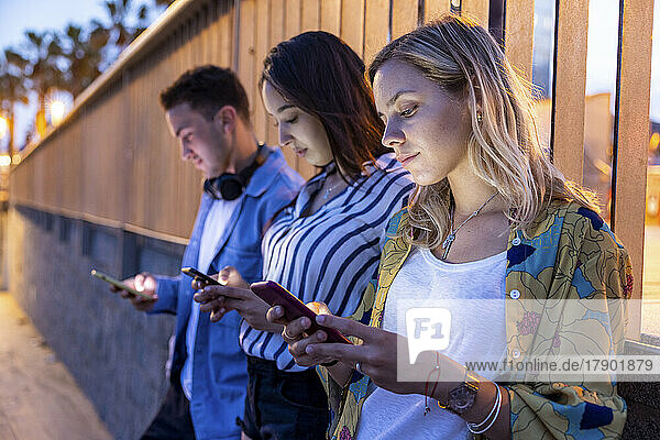 Young women and man surfing net through smart phones in front of railing at night