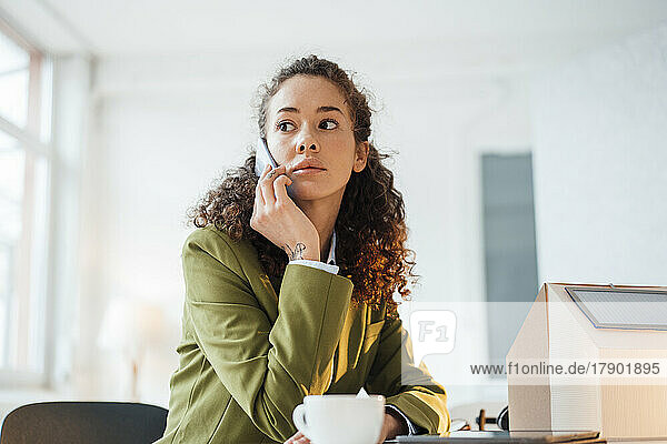 Geschäftsfrau sitzt am Schreibtisch im Büro und telefoniert mit ihrem Smartphone