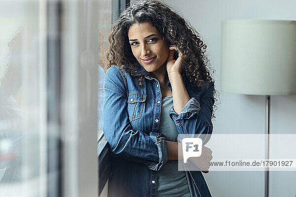 Happy woman with curly hair standing by window at home