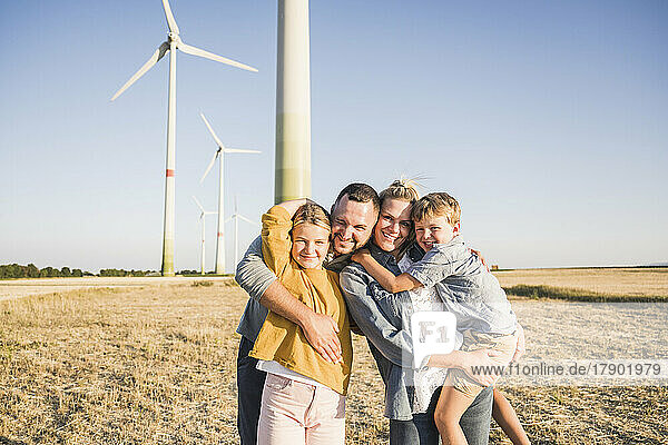 Glückliche Familie steht im Windpark und umarmt Kinder