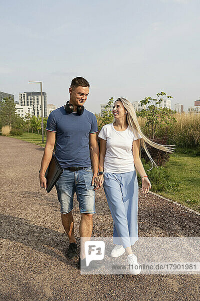 Happy boyfriend and girlfriend walking together holding hands in park