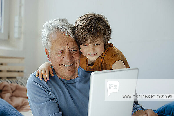 Smiling senior man taking selfie with grandson through tablet PC at home