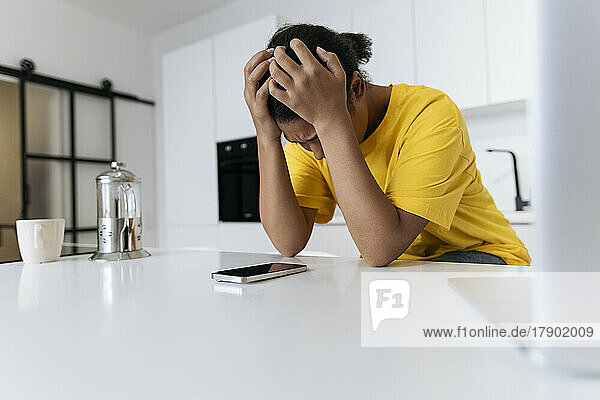 Unhappy woman sitting at the table in the kitchen with head in hands