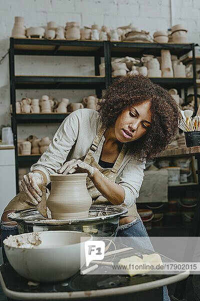 Young craftswoman molding pot shape on pottery wheel