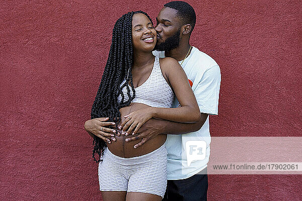 Boyfriend kissing pregnant girlfriend standing in front of wall