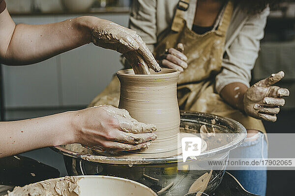 Hands of potter molding shape by woman in workshop