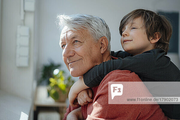 Thoughtful boy embracing grandfather from behind at home