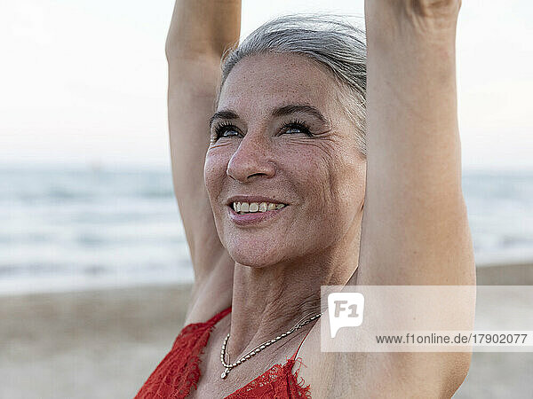 Glückliche ältere Frau mit erhobenen Händen am Strand