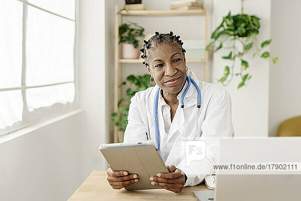 Lächelnde Ärztin mit Tablet-PC sitzt am Tisch im Heimbüro