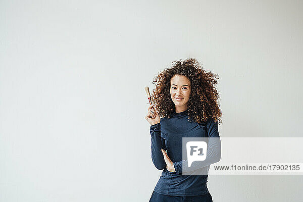 Smiling woman holding paintbrush in front of white wall