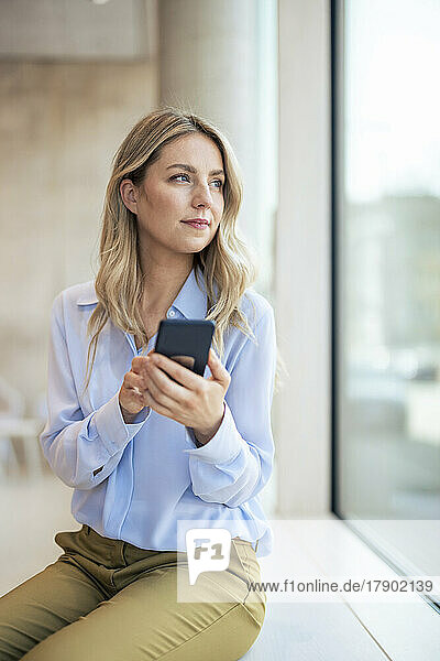 Thoughtful businesswoman with smart phone in office