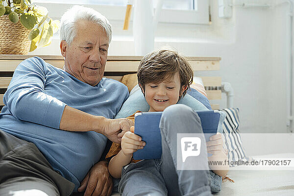 Lächelnder Junge teilt zu Hause Tablet-PC mit Großvater