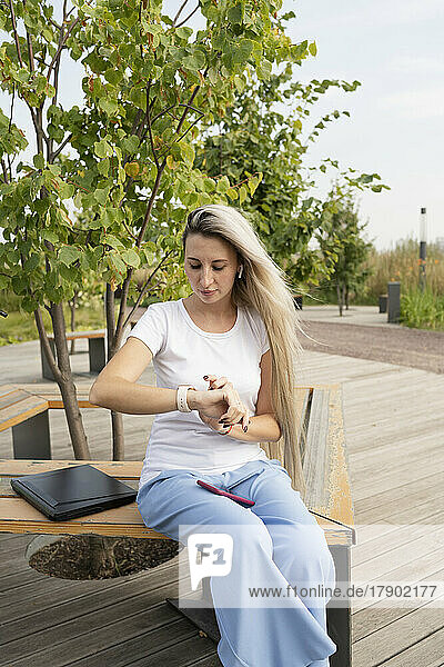 Young woman sitting and looking at her wristwatch in park