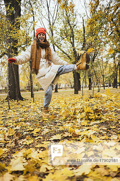 Happy young woman kicking autumn leaves at park