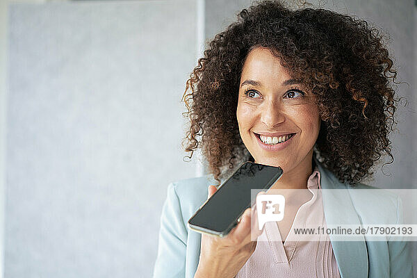Smiling businesswoman sending voicemail through smart phone