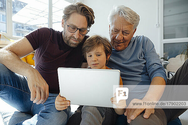 Boy watching movie with father and grandfather on tablet PC at home